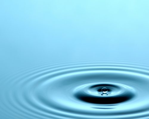 Close-up of a water droplet ripple on a pale blue surface